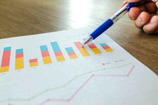 Detailed close-up of a hand pointing at colorful charts with a blue pen on wooden surface.